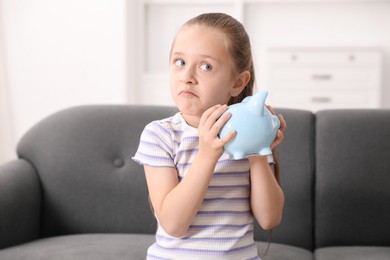 Photo of Pocket money. Little girl with piggy bank on sofa at home