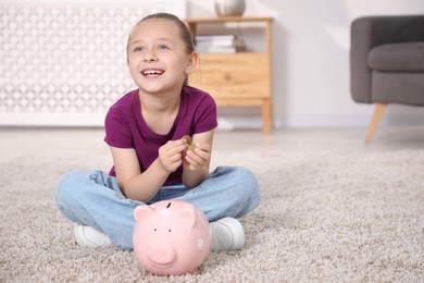 Photo of Little girl with pocket money and piggy bank on floor at home, space for text