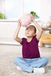 Photo of Pocket money. Little girl with piggy bank on floor at home