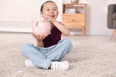 Photo of Pocket money. Little girl with piggy bank on floor at home, space for text