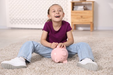 Photo of Pocket money. Little girl with piggy bank on floor at home