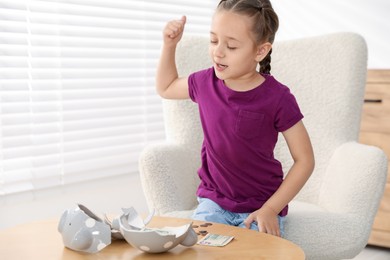 Photo of Little girl with pocket money and broken piggy bank at home, space for text