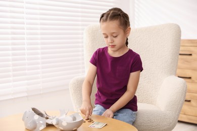 Photo of Little girl counting her pocket money at wooden table indoors, space for text