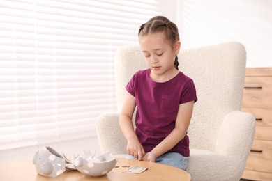 Photo of Little girl counting her pocket money at wooden table indoors, space for text