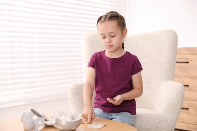 Photo of Little girl counting her pocket money at wooden table indoors, space for text