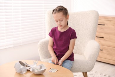 Photo of Little girl counting her pocket money at wooden table indoors