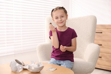 Photo of Little girl with pocket money in armchair at home, space for text