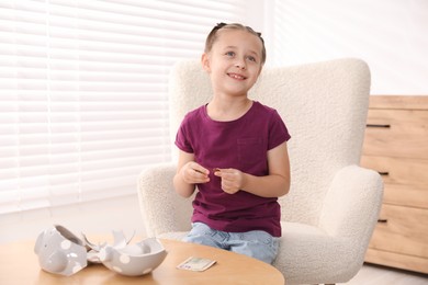 Photo of Little girl with pocket money in armchair at home, space for text