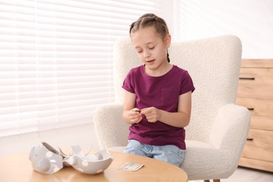 Photo of Little girl with pocket money in armchair at home, space for text