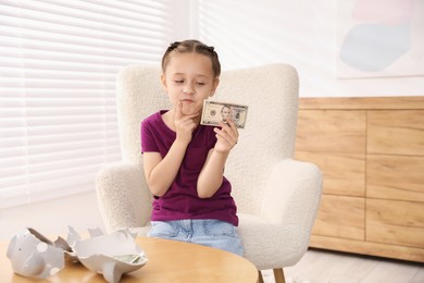 Photo of Little girl with pocket money in armchair at home