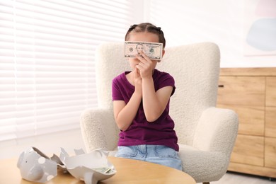Photo of Little girl with pocket money in armchair at home
