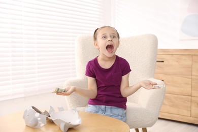 Photo of Little girl with pocket money in armchair at home