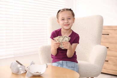 Photo of Little girl with pocket money in armchair at home