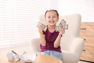 Photo of Little girl with pocket money in armchair at home