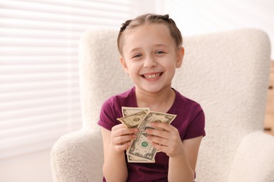 Photo of Little girl with pocket money in armchair at home