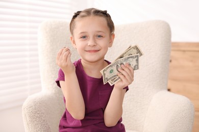 Photo of Little girl with pocket money in armchair at home