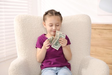 Photo of Little girl with pocket money in armchair at home