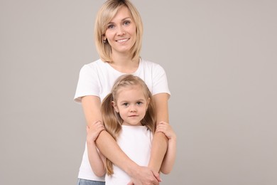 Family portrait of happy mother and daughter on grey background