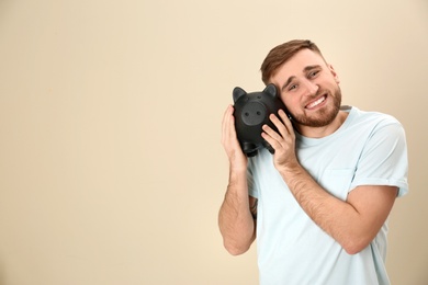 Photo of Happy young man with piggy bank and space for text on color background. Money saving