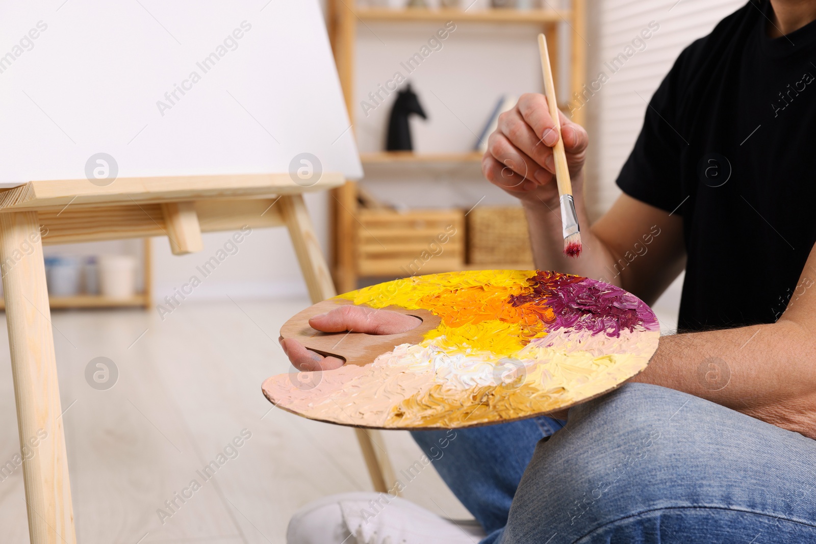 Photo of Man with brush and artist`s palette painting in studio, closeup. Using easel to hold canvas