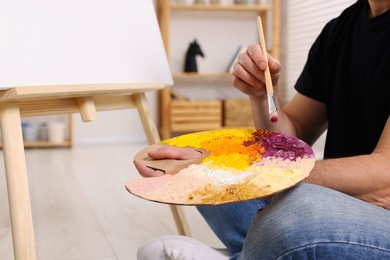 Photo of Man with brush and artist`s palette painting in studio, closeup. Using easel to hold canvas