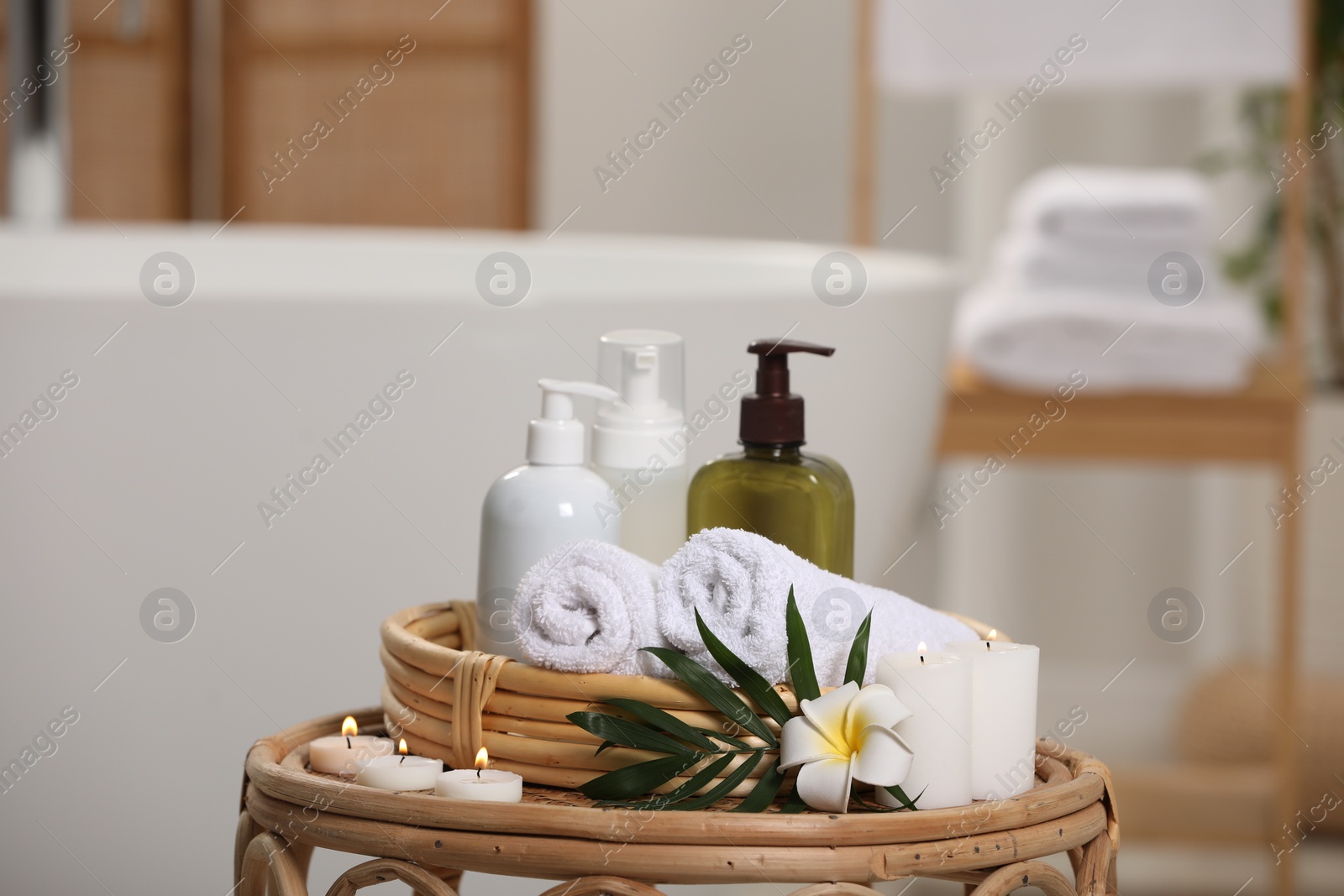 Photo of Spa products, burning candles, plumeria flower and tropical leaf on table in bathroom