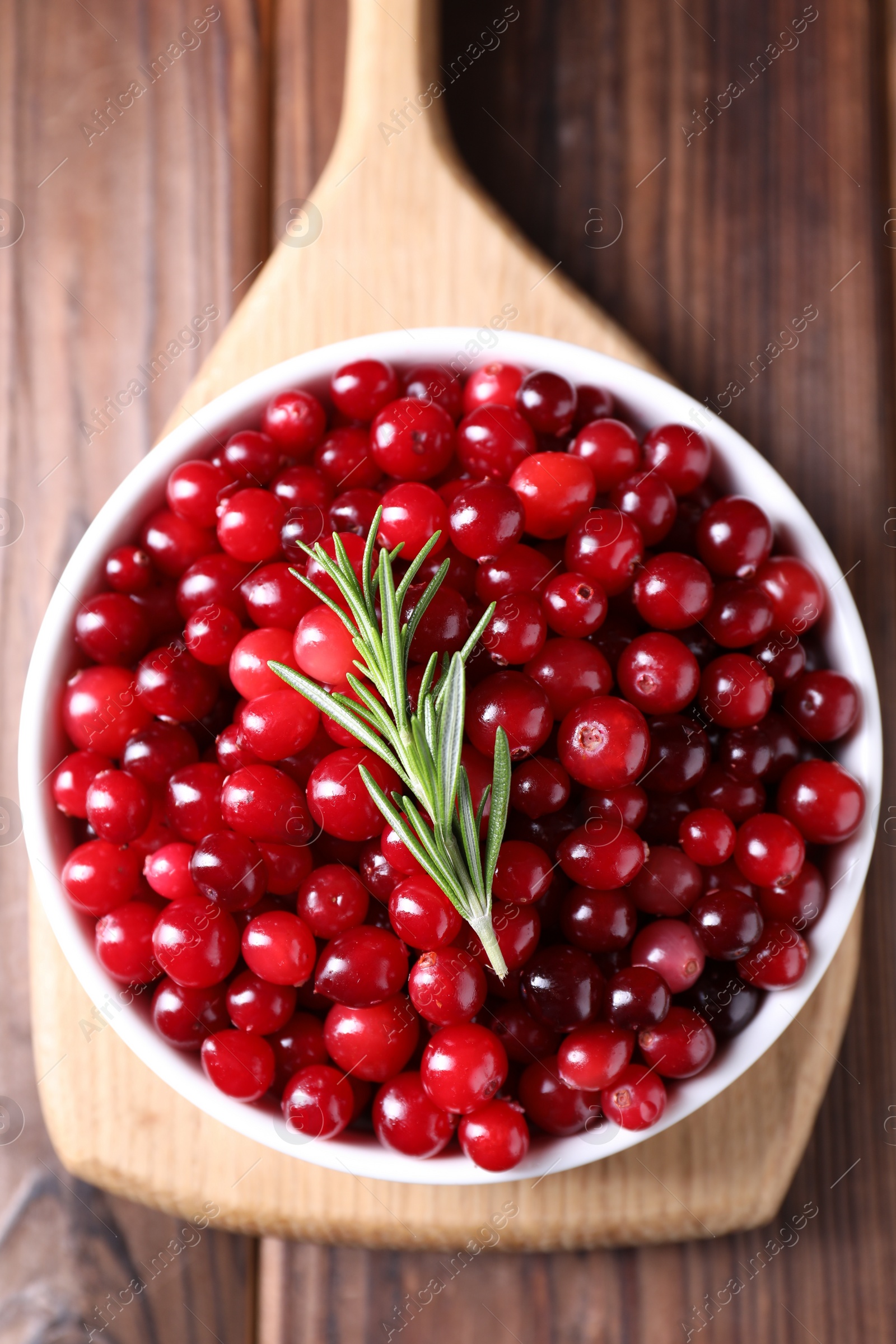 Photo of Fresh ripe cranberries and rosemary in bowl on wooden table, top view