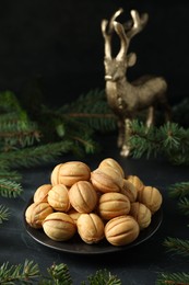 Plate of tasty nut shaped cookies among fir branches on black table