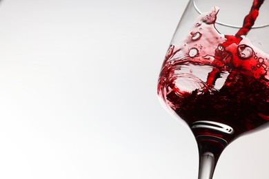 Photo of Pouring tasty red wine in glass on white background, closeup. Space for text