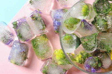 Ice cubes with flowers and glass bowl on color background, flat lay