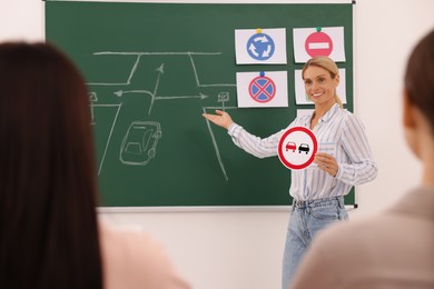 Teacher showing No Overtaking road sign near chalkboard during lesson in driving school
