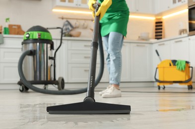 Photo of Professional janitor vacuuming floor in kitchen, closeup
