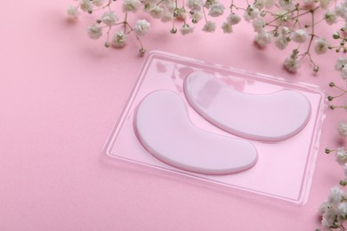 Photo of Package with under eye patches and flowers on light pink background, closeup. Cosmetic product