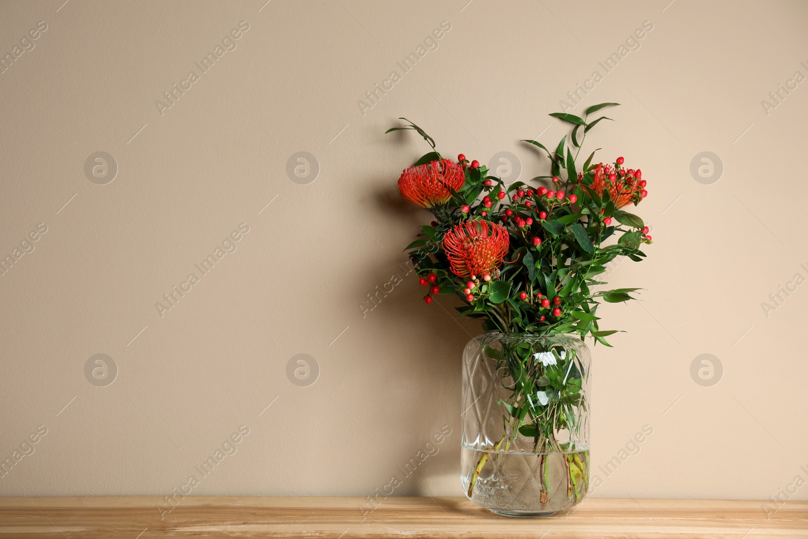 Photo of Bouquet with beautiful red protea flowers in vase on wooden table against beige background. Space for text