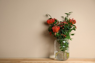 Photo of Bouquet with beautiful red protea flowers in vase on wooden table against beige background. Space for text