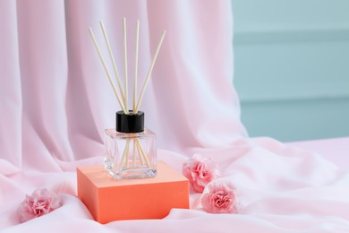 Photo of Stylish presentation of reed diffuser and roses on pink fabric. Space for text