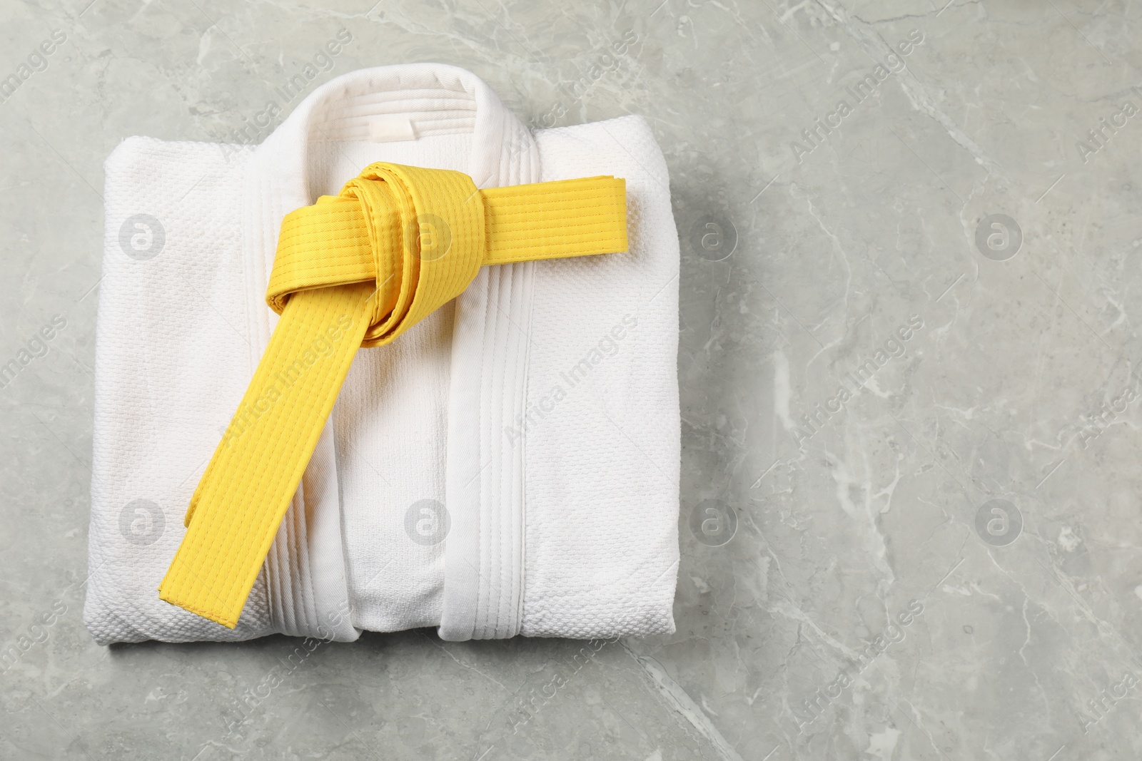 Photo of Yellow karate belt and white kimono on gray marble background, top view. Space for text