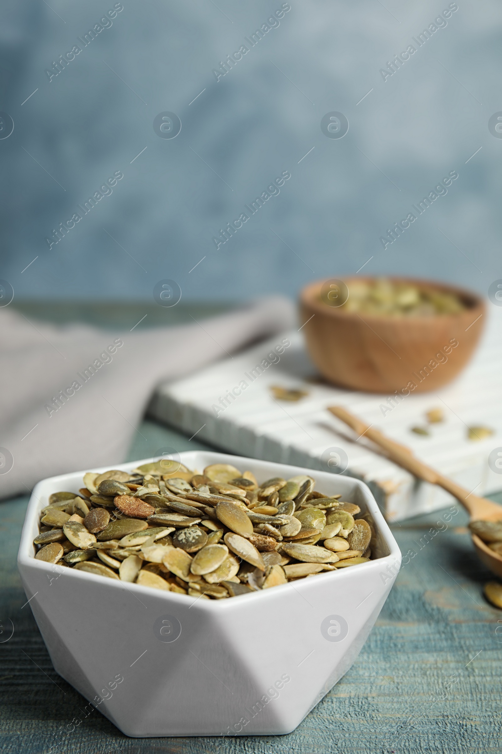 Photo of Bowl of raw pumpkin seeds on blue wooden table. Space for text