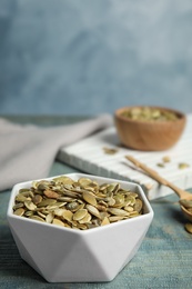 Photo of Bowl of raw pumpkin seeds on blue wooden table. Space for text