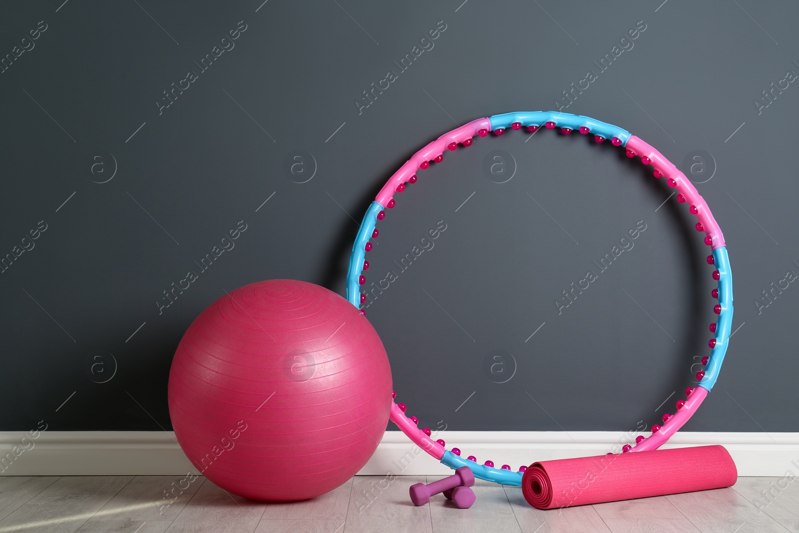 Photo of Hula hoop, exercise ball, yoga mat and dumbbells near grey wall in gym