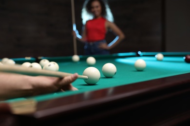 Photo of Young man playing billiard and blurred African-American woman on background, closeup