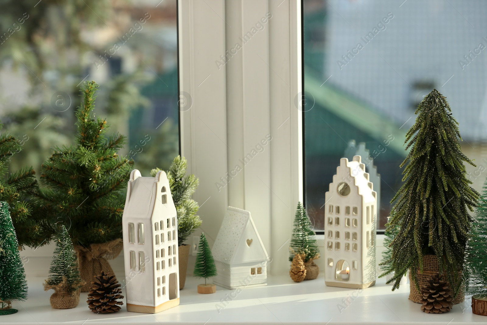 Photo of Beautiful house shaped candle holders and small fir trees on windowsill indoors