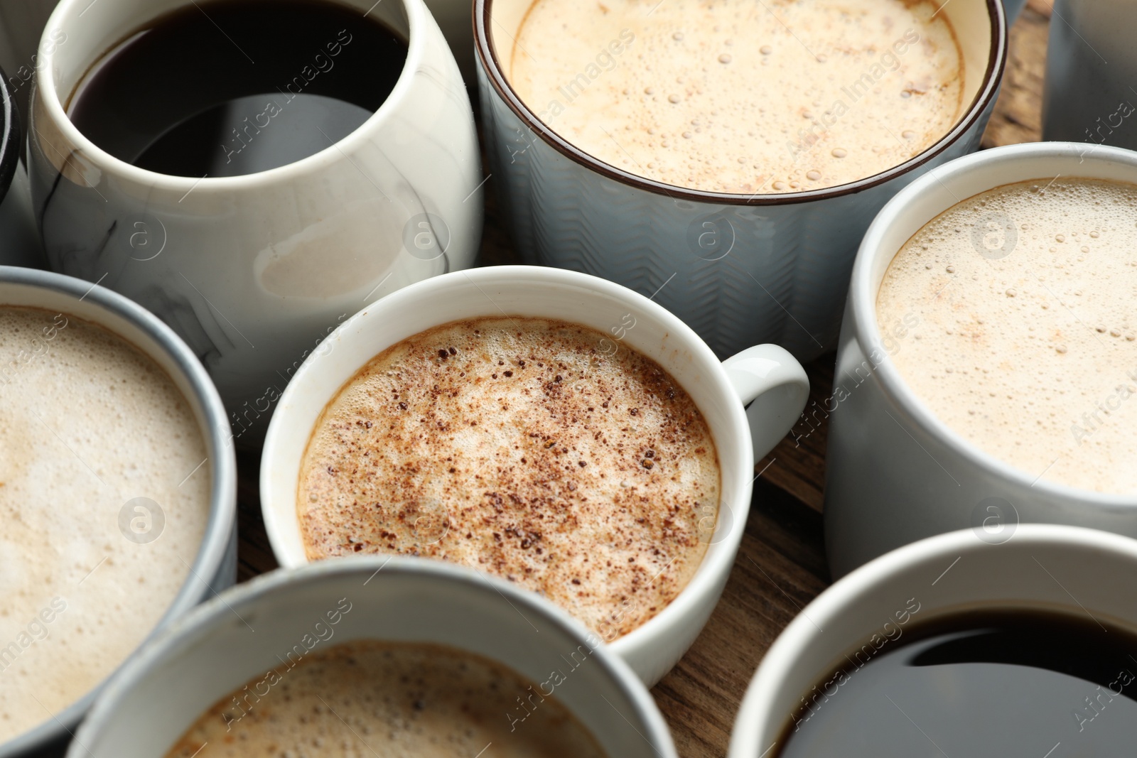 Photo of Many cups of different coffees on wooden table, closeup