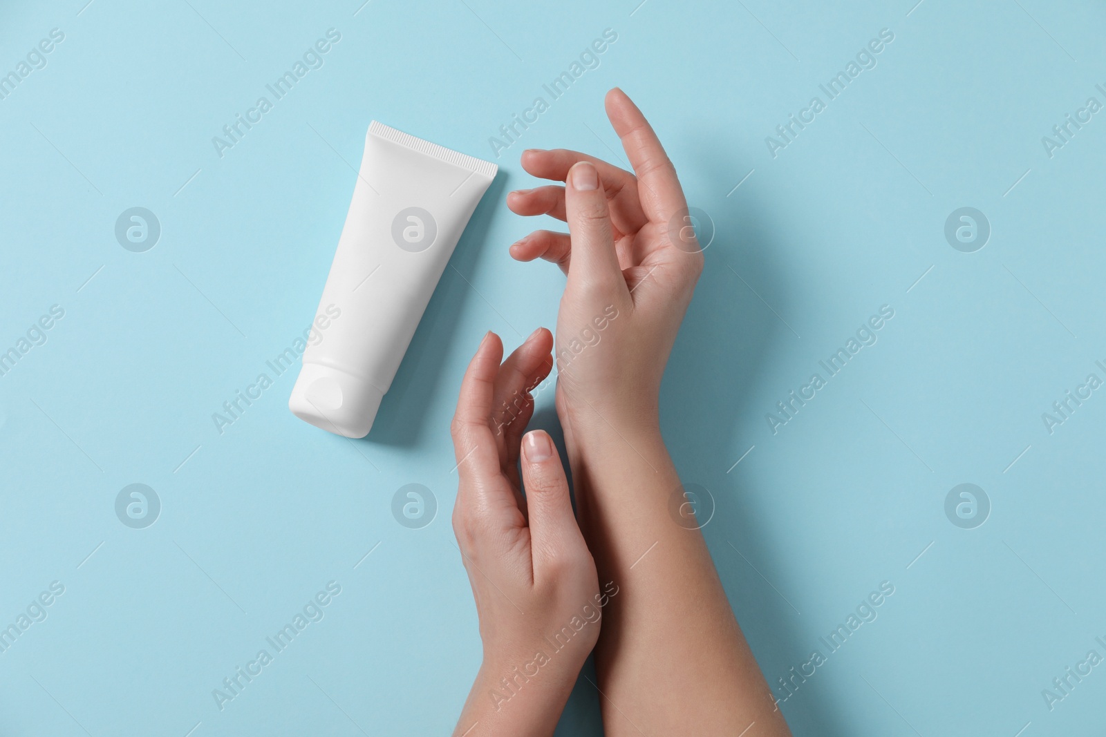 Photo of Woman with tube of hand cream on light blue background, top view