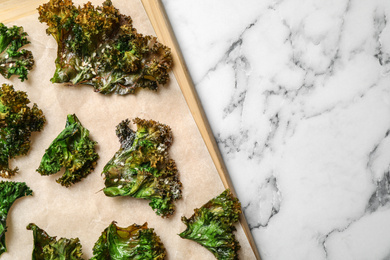 Photo of Tasty baked kale chips on marble table, top view. Space for text