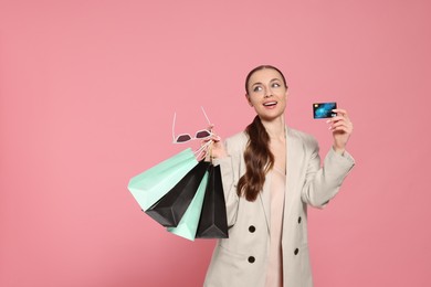 Photo of Stylish young woman with shopping bags and credit card on pink background