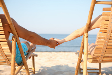 Photo of Couple holding hands while resting on sunny beach, closeup