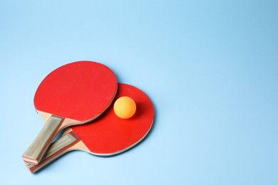 Ping pong ball and rackets on light blue background. Space for text