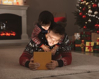 Image of Father and his cute son opening gift box with magical light on floor at home. Christmas celebration
