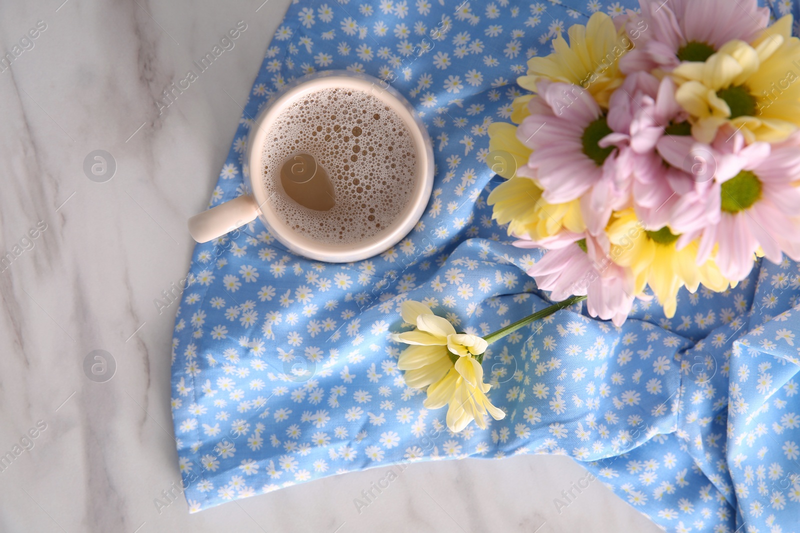 Photo of Cup of fresh coffee and beautiful bouquet on light blue printed cloth, top view. Good morning